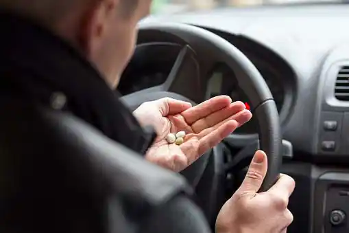 man sitting at the driver's seat and looking at the pills on his palm